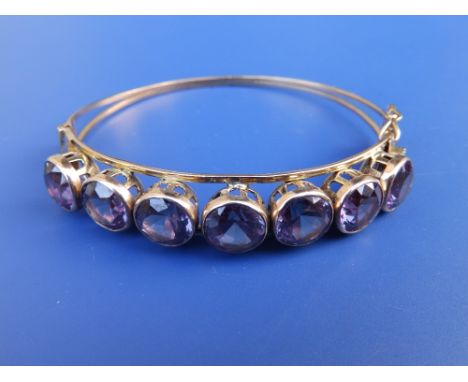 A yellow metal bangle set seven large synthetic stones.