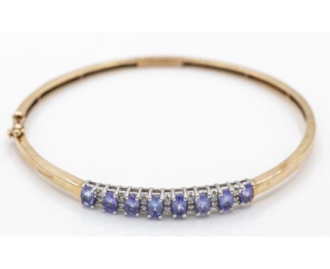 A hallmarked 9ct gold amethyst and diamond hinged bangle. The bangle being set with graduated oval mixed cut amethyst with tw