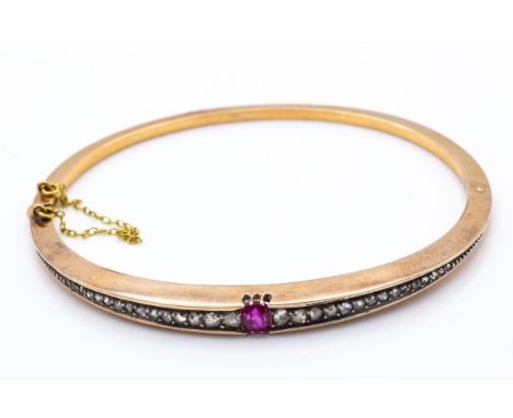 An antique 18ct gold ruby and diamond hinged bangle. The bangle set with a central ruby flanked by tapering channel set rose 