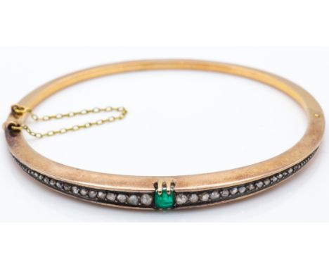 An antique 18ct gold emerald and diamond hinged bangle. The bangle set with a central emerald flanked by tapering channel set