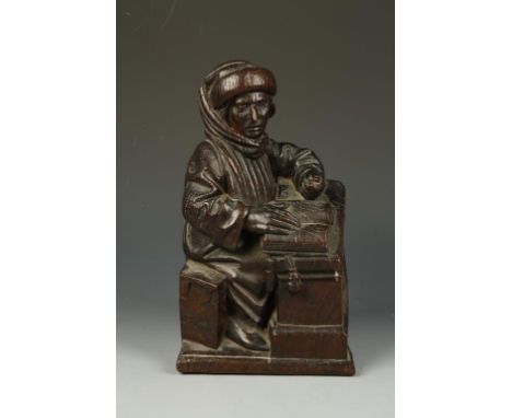 A CARVED OAK SCULPTURE OF A SEATED SCHOLAR, working at a open book at a desk, the scholar wearing hat and loose fitting cloak