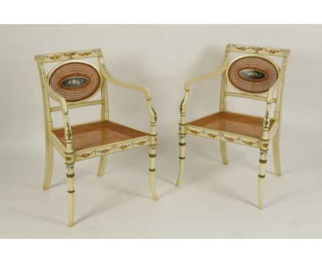 A PAIR OF REGENCY STYLE CREAM PAINTED ARMCHAIRS, each with cane-work oval backs with a central panel painted with a floral bo