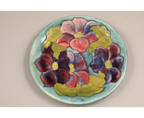 Moorcroft pottery shallow dish, decorated in clematis design, on light blue/green ground. Initialled WM to back. diameter 26c