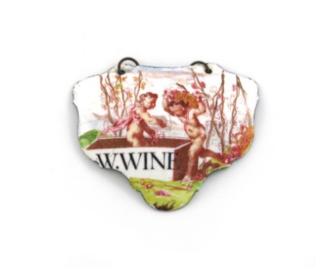 A rare mid 18th century Battersea enamel wine label, circa 1755, escutcheon form, with two cupids carrying and pressing grape