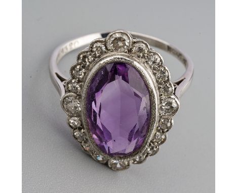 An amethyst and diamond cluster ring, set with an oval shape amethyst, within a single and early brilliant cut diamond border