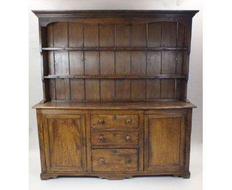 A waxed pine dresser, the canopied top with enclosed two shelf rack above a rectangular top and three central drawers, indent