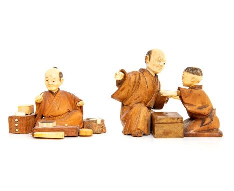 Two Japanese carved cedar wood and ivory okimono, one depicting a seated man in kimono, at a table with tool in hand, next to