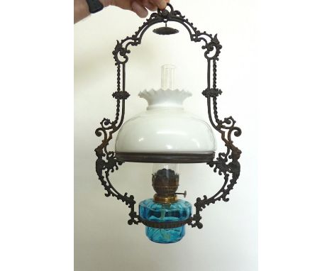 A Victorian hanging oil lamp with cast iron scrollwork frame, blue glass reservoir and white shade 