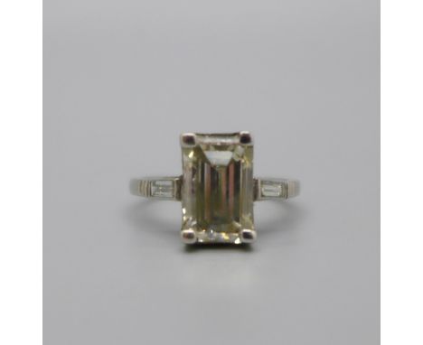 An emerald cut diamond ring set in platinum, approximately 3 carats diamond weight and with each shoulder set with a diamond,