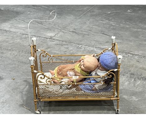 An early 20th century iron doll's cot 22" long; the lot to include three dolls.