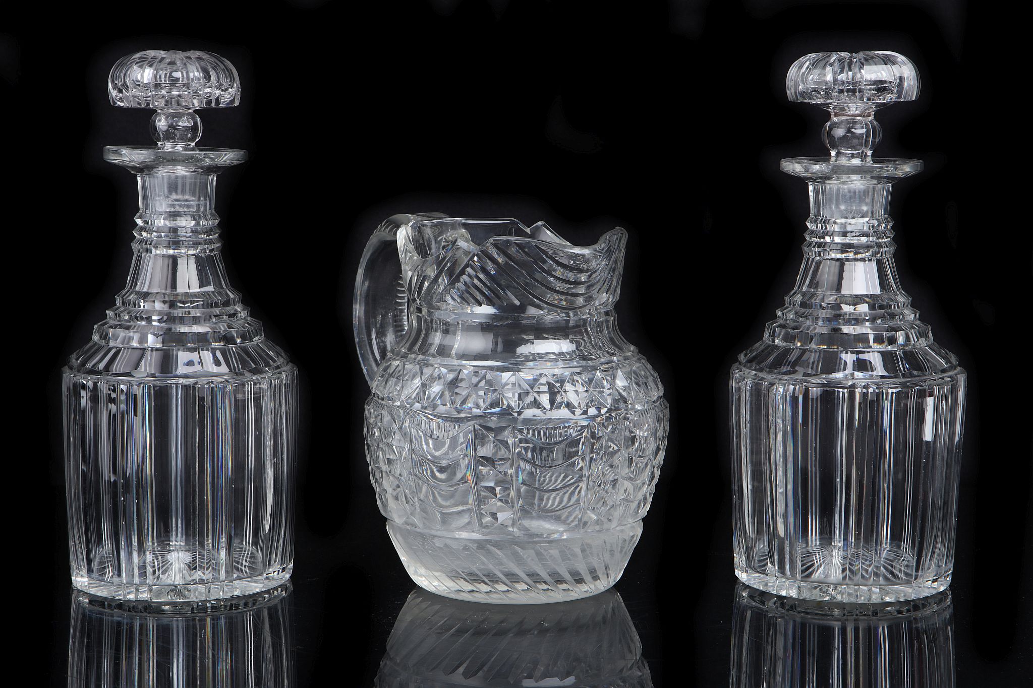A PAIR OF REGENCY CUT GLASS DECANTERS AND A WATER JUG, circa 182030, the decanters of typical fo