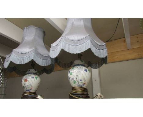 A pair of oriental style table lamps with fringed shades. ****Condition report**** No damage to pottery lamps or wooden bases
