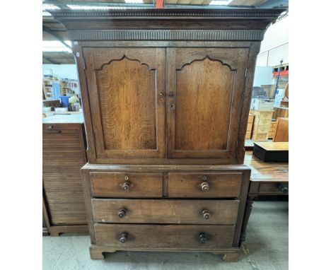An 18th century oak linen press, with a moulded dentil cornice above a pair of arched panelled doors, the base with two short