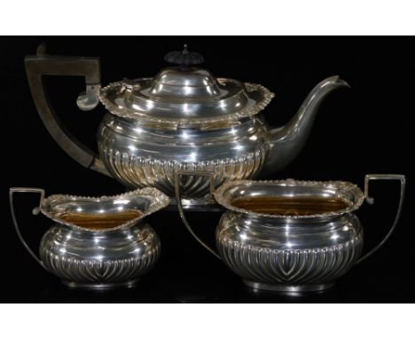 A George V silver three piece tea service, comprising teapot of cape form, two handled sugar bowl and milk jug, each partiall