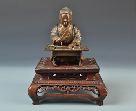 A Japanese 19th century detailed bronze figure of a kneeling scribe working at a low desk on a square hardwood stand, in the 