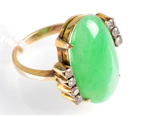 A yellow gold ring set an oval jade cabochon, flanked by a seven diamond cross over.