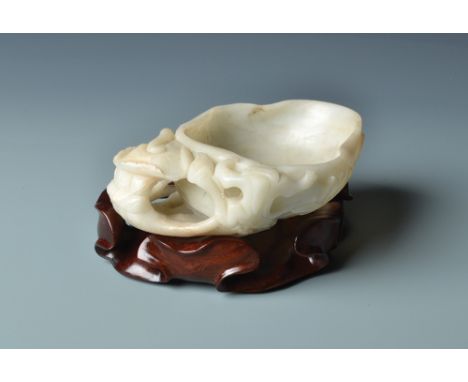 An 18th century Chinese celadon jade brush washer carved as a large curled lotus leaf resting upon numerous stalks and a lotu