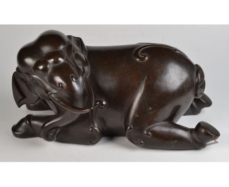 An early 20th century Chinese stylised bronze of a kneeling elephant looking over his left shoulder, height 26cm, length 52cm