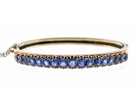 A sapphire and 14ct gold hinged bangle, set with a row of seventeen graduated oval claw set sapphires, the largest approx 5 x