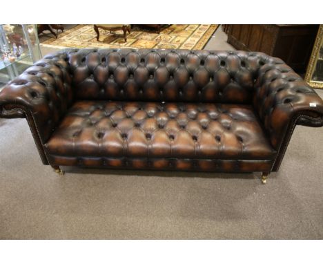 A contemporary brown leather chesterfield sofa. With a deep button back and arms with decorative metal stud detail, raised on