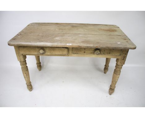 A vintage pine kitchen table. With a plank top and distressed paintwork, raised on turned supports, with two drawers, H74cm x