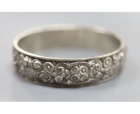 A continental white metal hinged bangle, decorated with continuous band of flowers and scrolls, 19 grams.