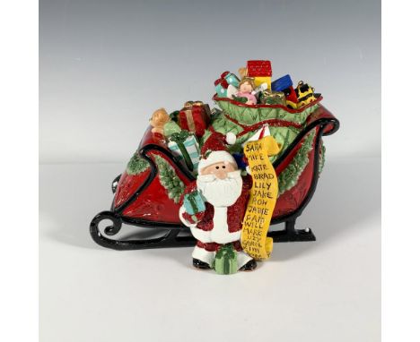 This whimsical sleigh figure depicts Santa Claus holding a list of names and a bag overflowing with gifts. A winder located a