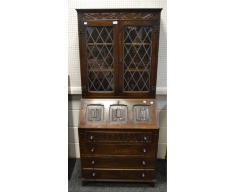 A Jacobean Revival oak bureau bookcase, carved scrolls to frieze, two astral glazed cupboard doors enclosing two shelves, the