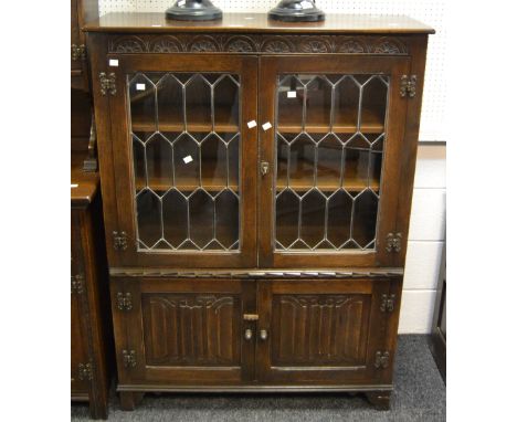A Jacobean Revival oak side cupboard, two astral glazed cupboard doors enclosing two shelves, the frieze carved with half-moo