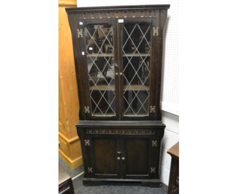 A Jacobean Revival oak corner cabinet, two astral glazed doors enclosing two shelves, the base with two cupboard doors enclos