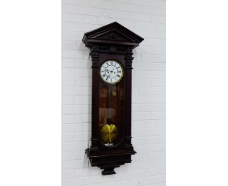 A stained dark wood wall clock, the architectural top over a glazed door enclosing an enamel dial with Roman numerals, comple