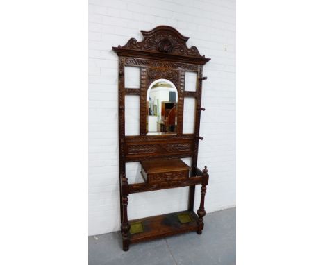 A carved oak hall stand, with arched top over a central mirror back above a glove box, flanked by stick holders and turned su