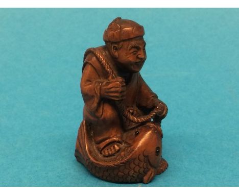 A carved wooden Netsuke in the form of a man catching a fish
