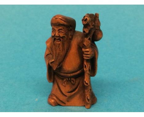 A carved wooden Netsuke in the form of a man holding a staff