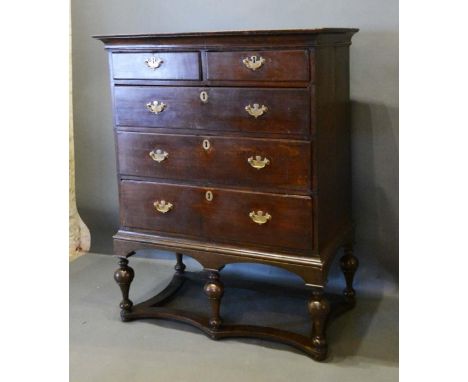 A George III Oak Chest on Stand, the moulded top above two short and three long graduated drawers with brass handles and escu