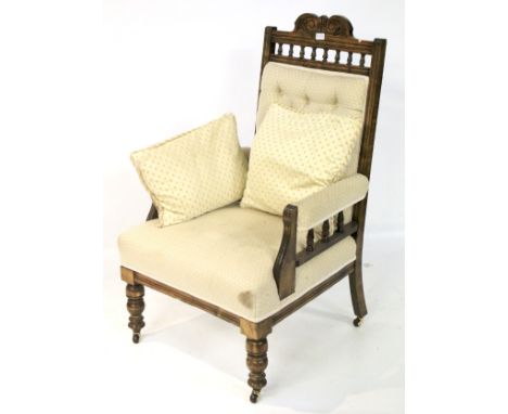 An oak framed, upholstered armchair. The back with carved and spindle details, upholstered in patterned cream fabric with a b