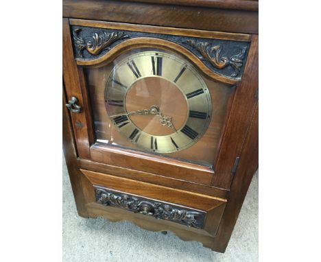 A wall clock the brass dial with Roman numerals with cupboard and drawer under.