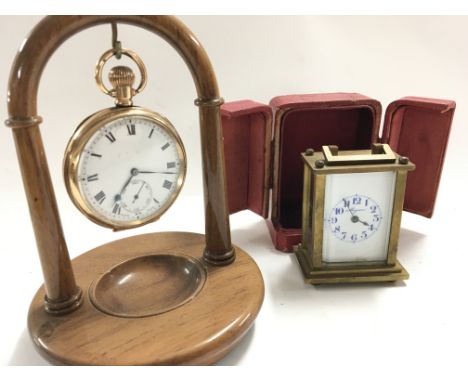 A gold plated open faced pocket watch on a watch stand seen working and a small talking brass cased carriage clock.