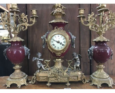 A gilt metal clock set of classical influences the clock flanked by cherubs, with a matching pair of candelabra.