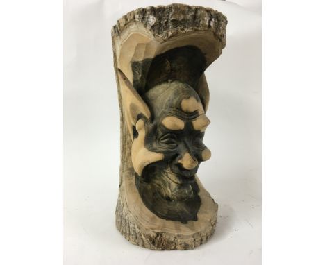 A carved head of a smiling figure with large pointed ears, carved out of a tree trunk