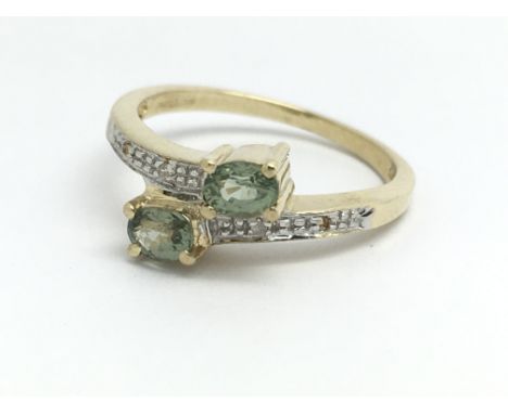 A 9ct yellow gold ring, with two pale green coloured stones, and a row of small diamonds on the shoulders, ring size approx J