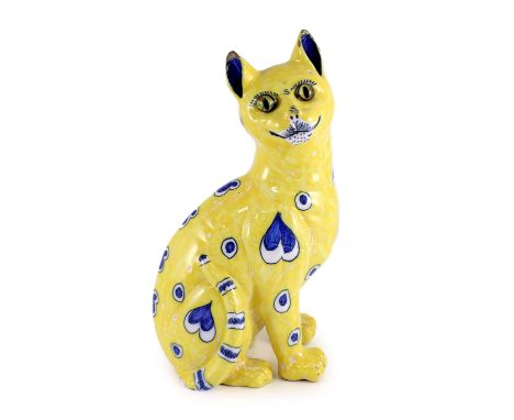 A Gallé yellow faience model of a seated smiling cat, c.1885,with applied glass eyes, decorated in blue with heart and teardr