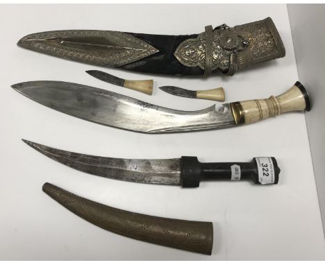 A vintage Gurkha kukri with typical curved blade and carved bone handle with brass finial housed in a pierced white metal mou