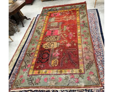 A Khotan carpet, the central panel set with vase design on a red ground, within a stepped mustard and taupe floral decorated 