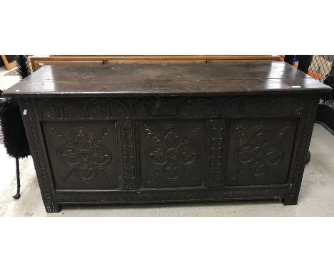A 17th Century oak coffer, the plank top with notch carved ends and moulded front edge over a lunette carved frieze and three