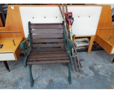 A wrought iron garden chair with wooden slats and a variety of garden tools