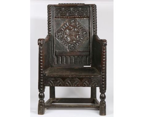 An 18th Century and later oak armchair, the scroll carved cresting rail above a stylised foliate carved panel back flanked by