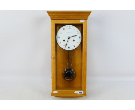 A contemporary Comitti Of London light oak cased wall clock with key and pendulum, approximately 50 cm. [W]