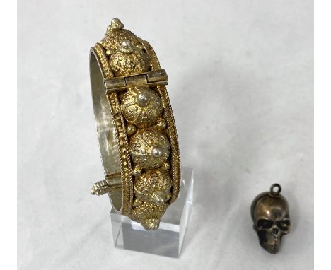 An unusual skull pendant containing miniature dice; a Middle Eastern hinged bangle in ornate white metal. 2.9cm high. Not tes