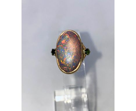 A yellow metal dress ring set large oval black opal coloured stone, flanked by 2 green stones, stamped '9ct', 7.6 gm size 'P'